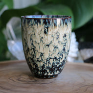 Handmade ceramic tea cup thats cream and blue reactive glaze and handleless