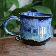 Handmade ceramic mug with a large handle, featuring a Black with a blue drip glaze.